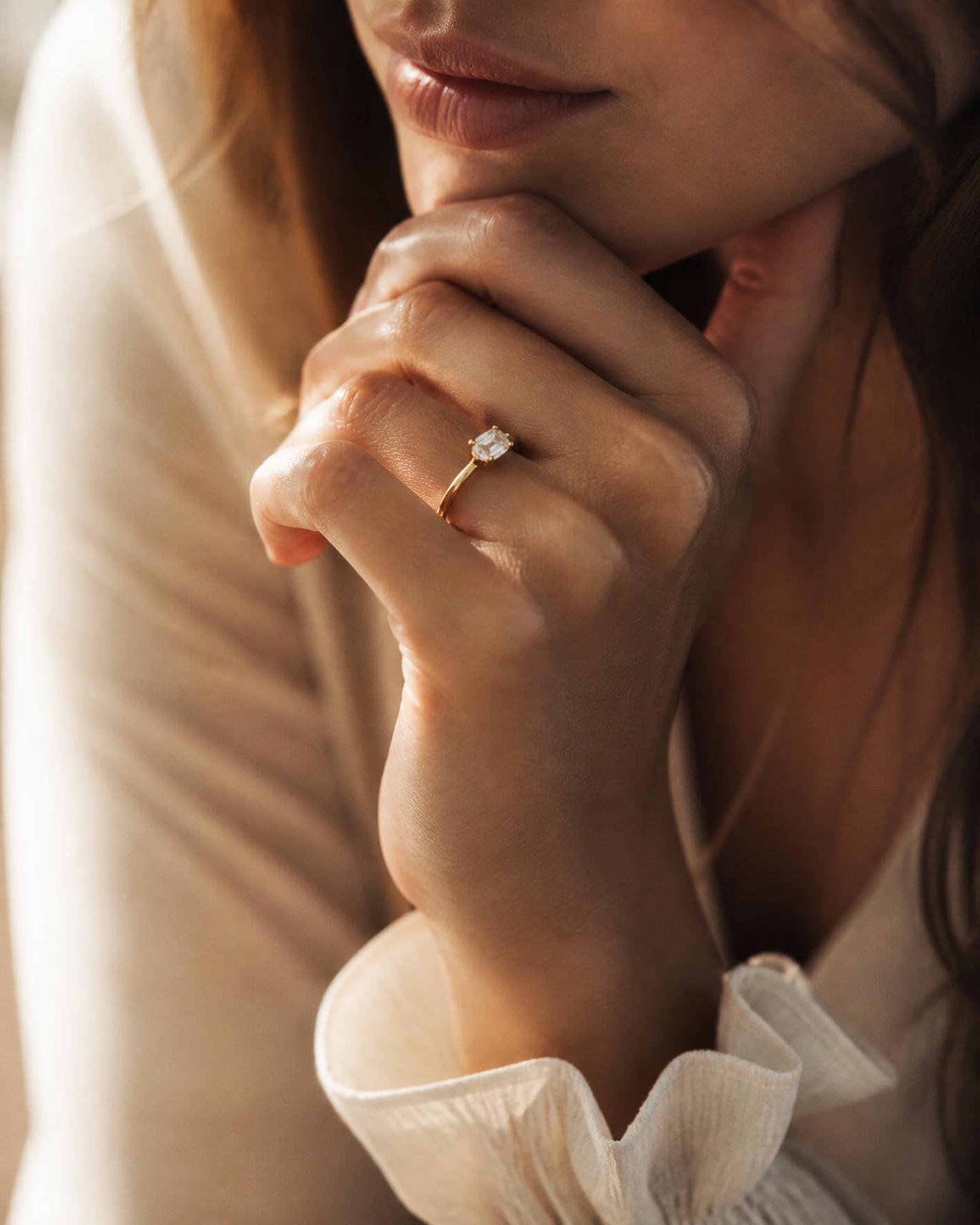 Hand wearing a slim gold solitaire engagement ring in warm daylight